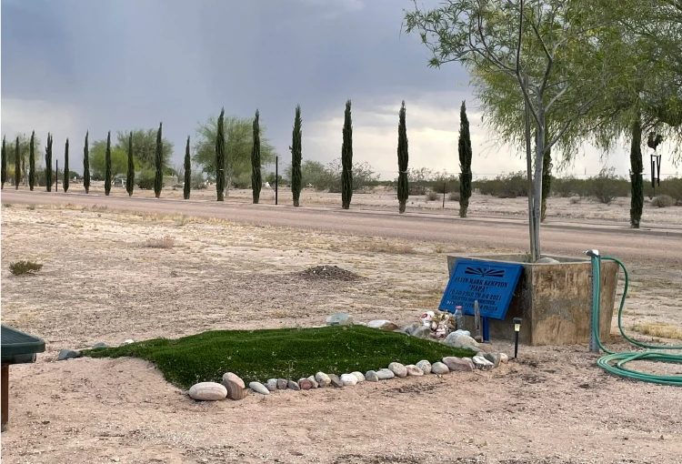A small grass-covered grave plot bordered with stones at Florence Memorial Park with a green garden hose connected to a spigot beside it an example of the kind of water hookup families have installed at the cemetery