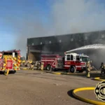 Fire engines and firefighters respond to the WM transfer station fire in Casa Grande, spraying water into a smoke-filled loading bay.