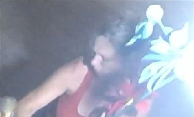 Nighttime surveillance image of a person in a red tank top with shoulder-length hair shown near illuminated yard decorations