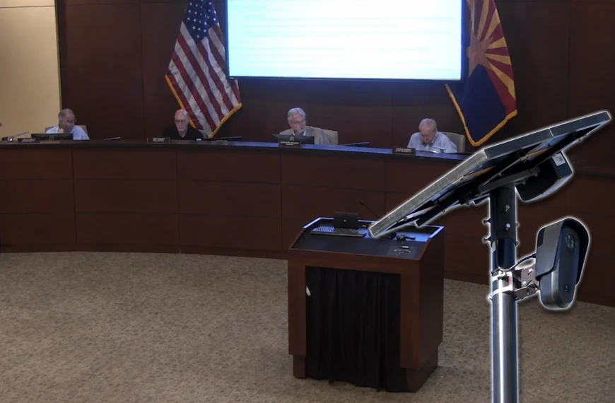 A Flock Safety license plate reader camera on a solar-powered pole appears in the foreground while four Pinal County supervisors sit at the dais during the Aug. 12 meeting.