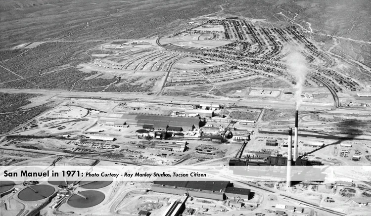 Black-and-white 1971 aerial photo of San Manuel Arizona The towns curving residential streets fill the upper part of the frame while below them sprawls the copper ore-processing complex on the Ore Town Solar site with industrial buildings circular tanks and a tall smokestack trailing smoke