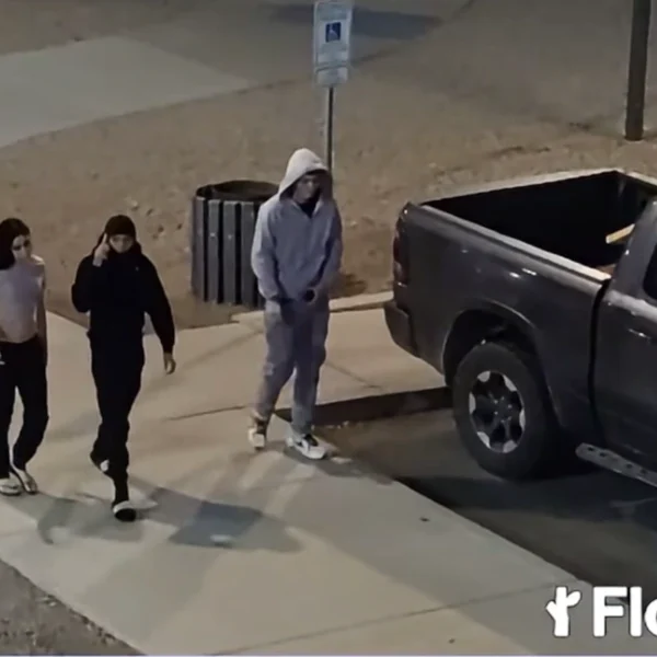 Three people walking on a sidewalk at night beside a parked pickup truck, in surveillance video released by police after a Casa Grande shooting.