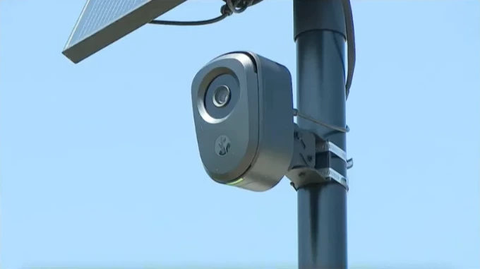 A solar-powered Flock Safety Falcon license plate reader mounted on a roadside pole.