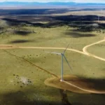 Aerial view of wind turbines spread across open grassland beneath distant hills