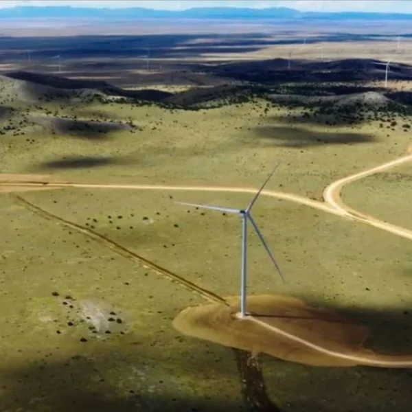 Aerial view of wind turbines spread across open grassland beneath distant hills