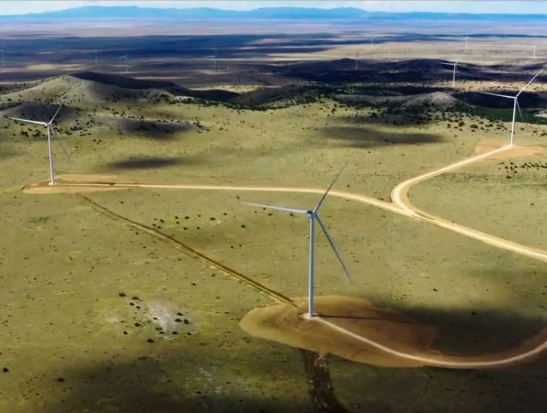 Aerial view of wind turbines spread across open grassland beneath distant hills
